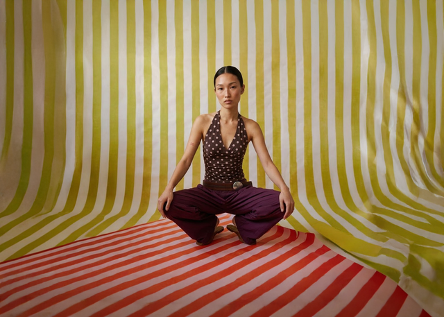 Woman sitting in a meditative pose on a striped floor with a yellow and white striped wall.